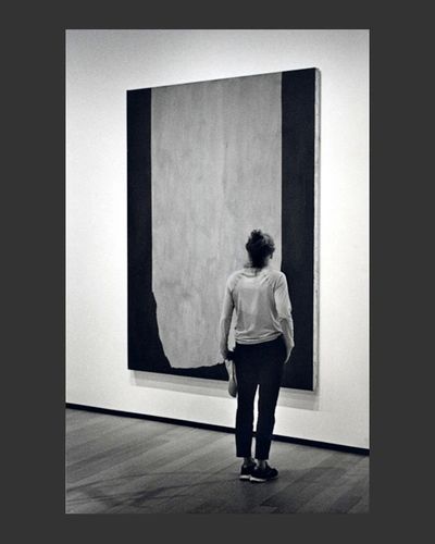 Young woman stands before a large abstract painting, her clothing and stance echoing the design sche