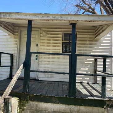 Worn front porch of an old white wooden house with dark railings.