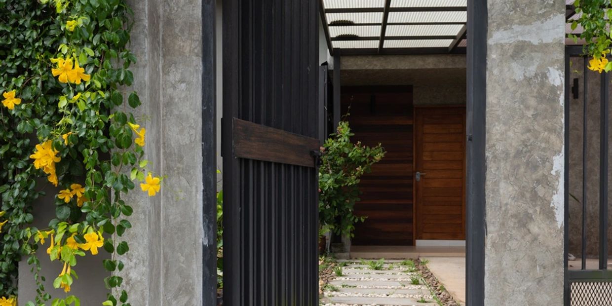 Open black gate with yellow flowers and wooden door in background.