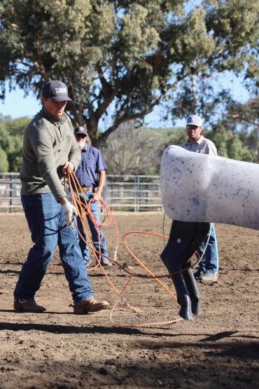 Man practicing lassoing on a mechanical horse in an outdoor arena.