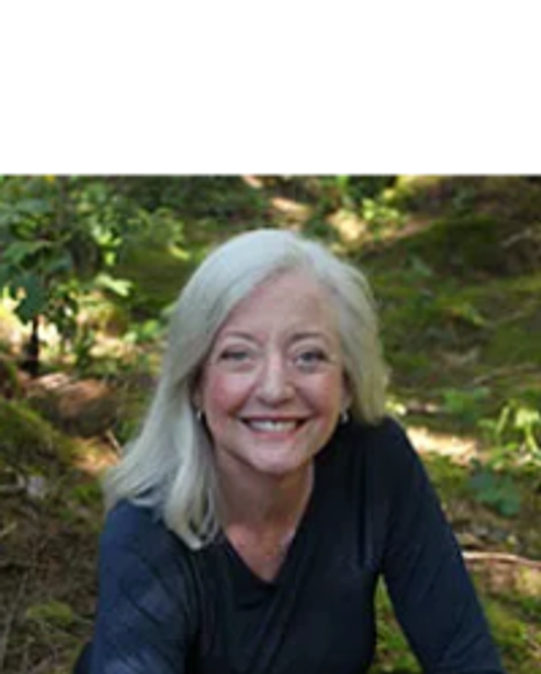 Smiling woman with white hair in a forest setting.
