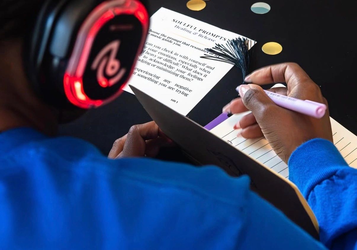 Person writing with headphones on.