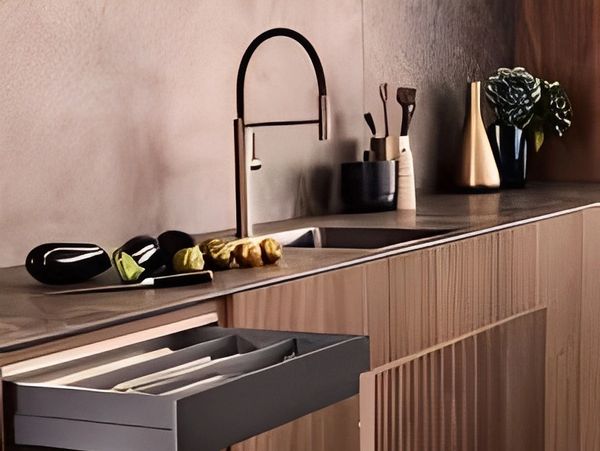 Modern kitchen with wood cabinets, dark faucet, and open utensil drawer.