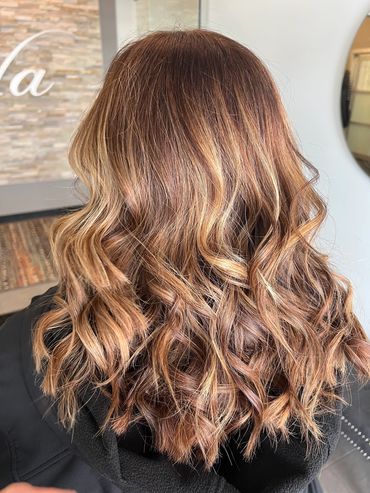 A rich brunette base with warm caramel blonde highlights, styled in loose curls
