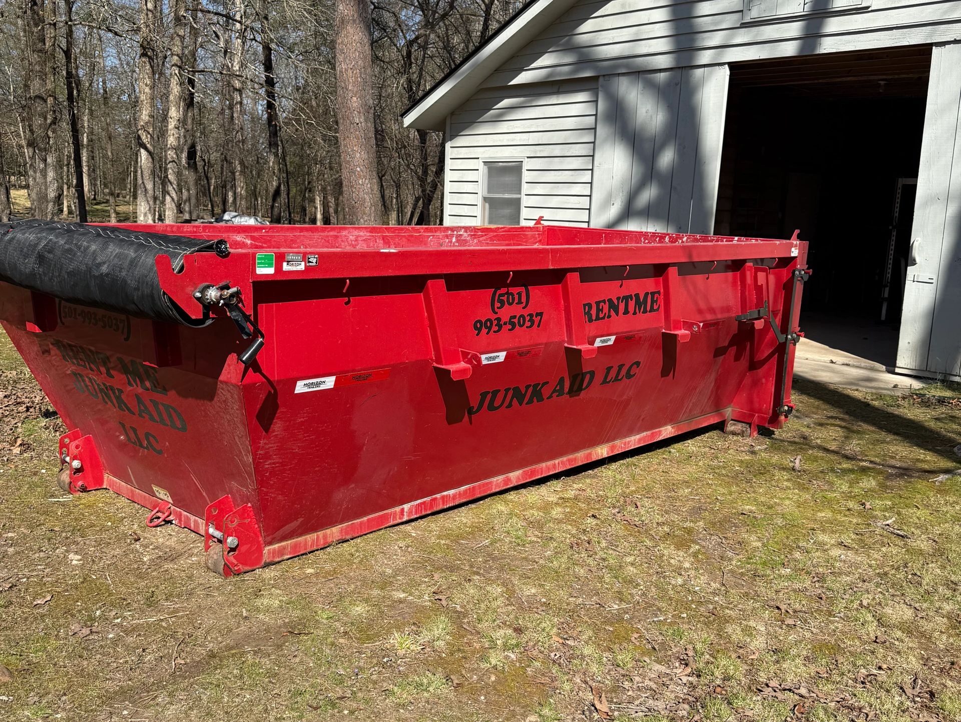Large red rental dumpster outside a white building.