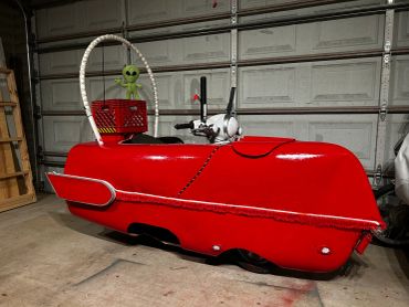 A shiny red custom vehicle with an alien toy in a crate at the back.