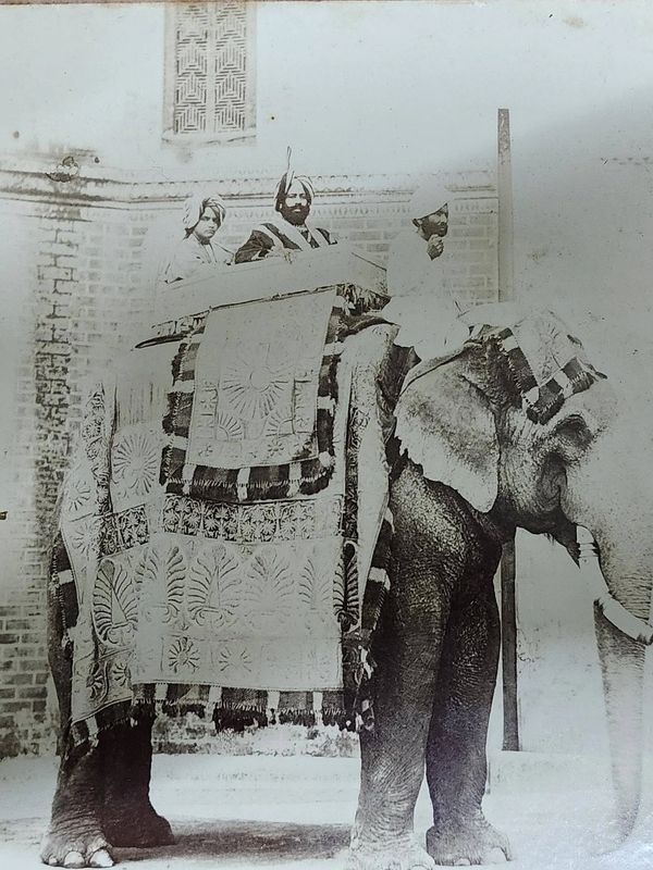 Vintage photo of three men in traditional attire riding a decorated elephant.