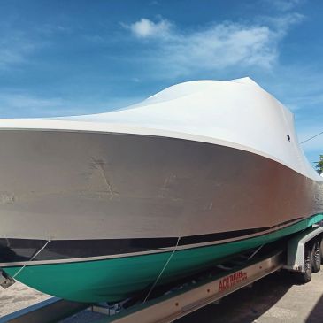 Large white and green boat on trailer under blue sky.