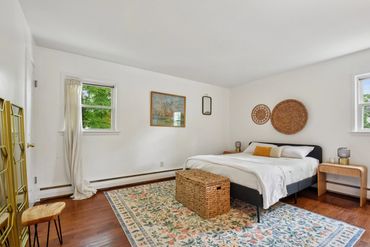 Bright bedroom with hardwood floors, floral rug, and wicker accents.