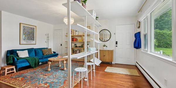 Bright living room with blue sofa, colorful rug, and open shelving.