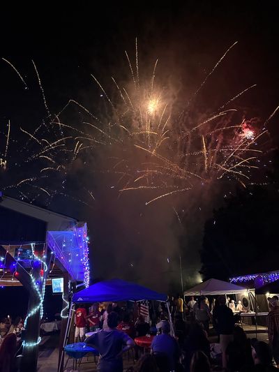 Fireworks light up the night sky above a festive crowd and decorated tents.