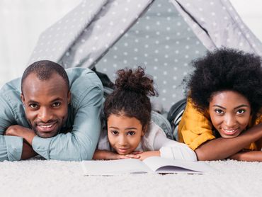 Parents are on the bed with their daughter with an open book on the bed.