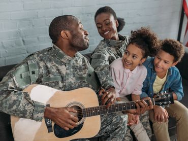 Dad playing the guitar for the wife and two children, Parents have on army uniforms