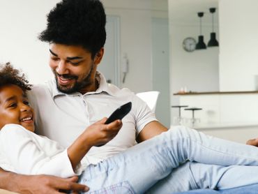 Dad is in a chair lounging while holding his daughter in his arms