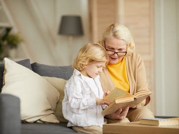 Grandmother is spending time with grandchild. She is showing the child something in a book