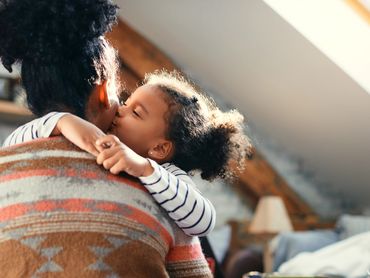 Toddler is hugging the mom and kissing her on the cheek.