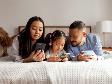 Asian parents with their daughter in the bed, All with their mobile devices.
