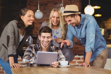 Friends at a coffee shop hovering over a computer. All are laughing