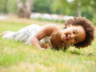 Young black child rolling in the grass with a huge smile.