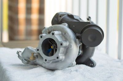 Close-up of a metallic turbocharger on a white surface.
