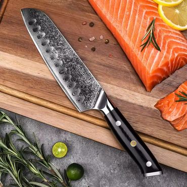 Damascus steel knife on cutting board with fresh salmon and herbs.