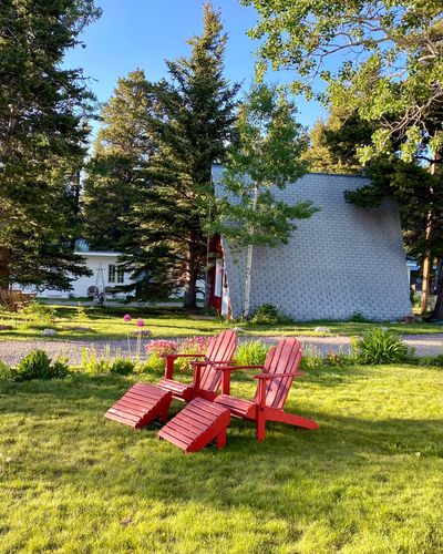 Two red Adirondack chairs on a lawn with red A-Frame in background 