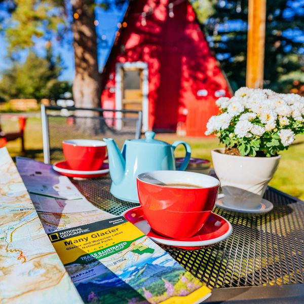 Two red cups, a blue teapot, maps and flowers on metal table outside in front of red AFrame