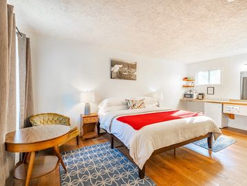 Hotel room with bed and red blanket, blue throw rug and small table with green chair