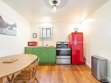 Cottage kitchen with green cabinets and red refrigerator and small wooden kitchen table