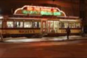 A vintage streetcar at night with illuminated signs and a person nearby.