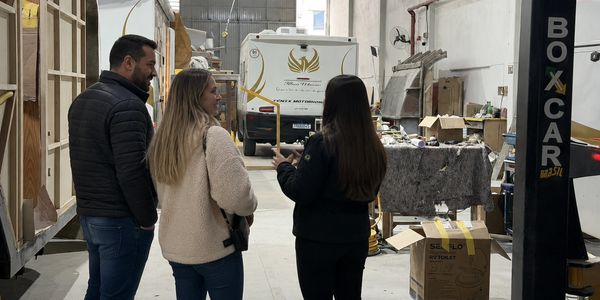 Three people discussing inside an industrial warehouse filled with various items and boxes.