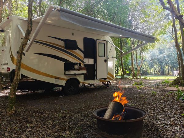 RV parked in a forest with a campfire burning nearby.