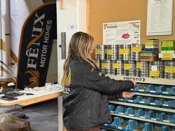 Person organizing hardware supplies in a workshop with Fênix Motor Homes banner.