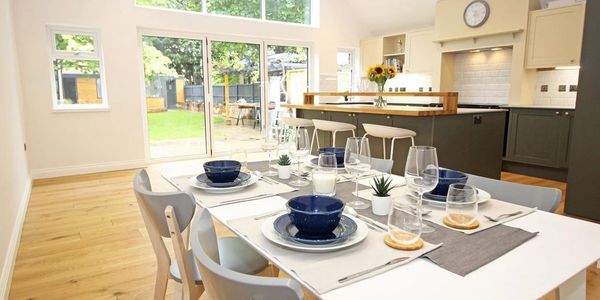 Bright dining area with modern table setting and open kitchen overlooking a garden.