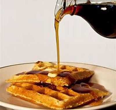 Pouring pure maple syrup over a stack of waffles, one of the many reasons to choose Wisconsin pure maple syrup