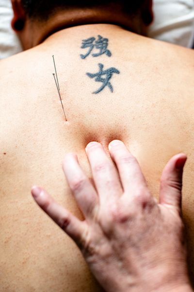 Patient laying face down. Two Chinese characters tattooed on upper back. Alex is palpating vertebrae