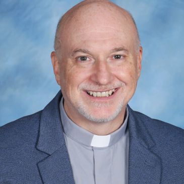 Smiling middle-aged man with clerical collar and suit jacket.