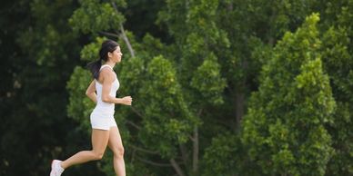 A woman jogging outdoors surrounded by lush green trees.