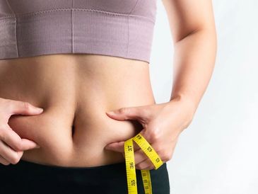 a woman holding a measuring tape while pinching her belly fat.