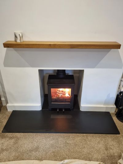 Cozy fireplace with a wooden mantel and single small white object on top.