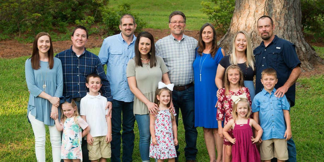 A large family group posing outdoors on a grassy area with smiles.
