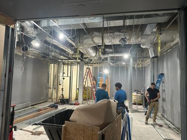 Three workers in a construction site with exposed ceiling ducts and ladders.
