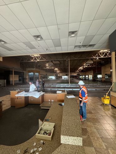 Construction workers inspect a large, empty indoor space with counters and tiled floors.
