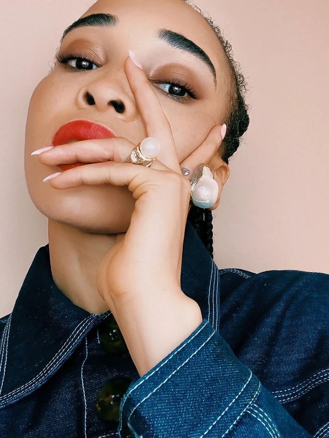 Close-up of a woman with red lipstick, pearl rings, and denim jacket.