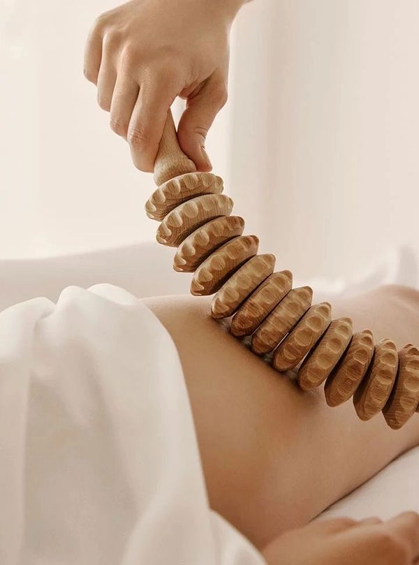 Wooden massage roller being used on a person's back during a spa treatment.