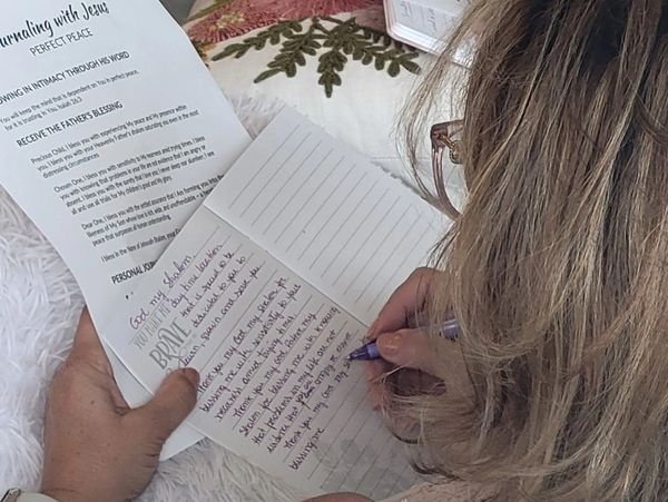 Person writing notes while holding a paper on journaling with Jesus.