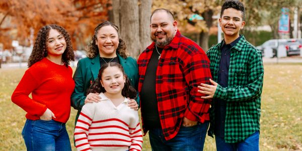 Family of five posing outdoors in fall clothing.