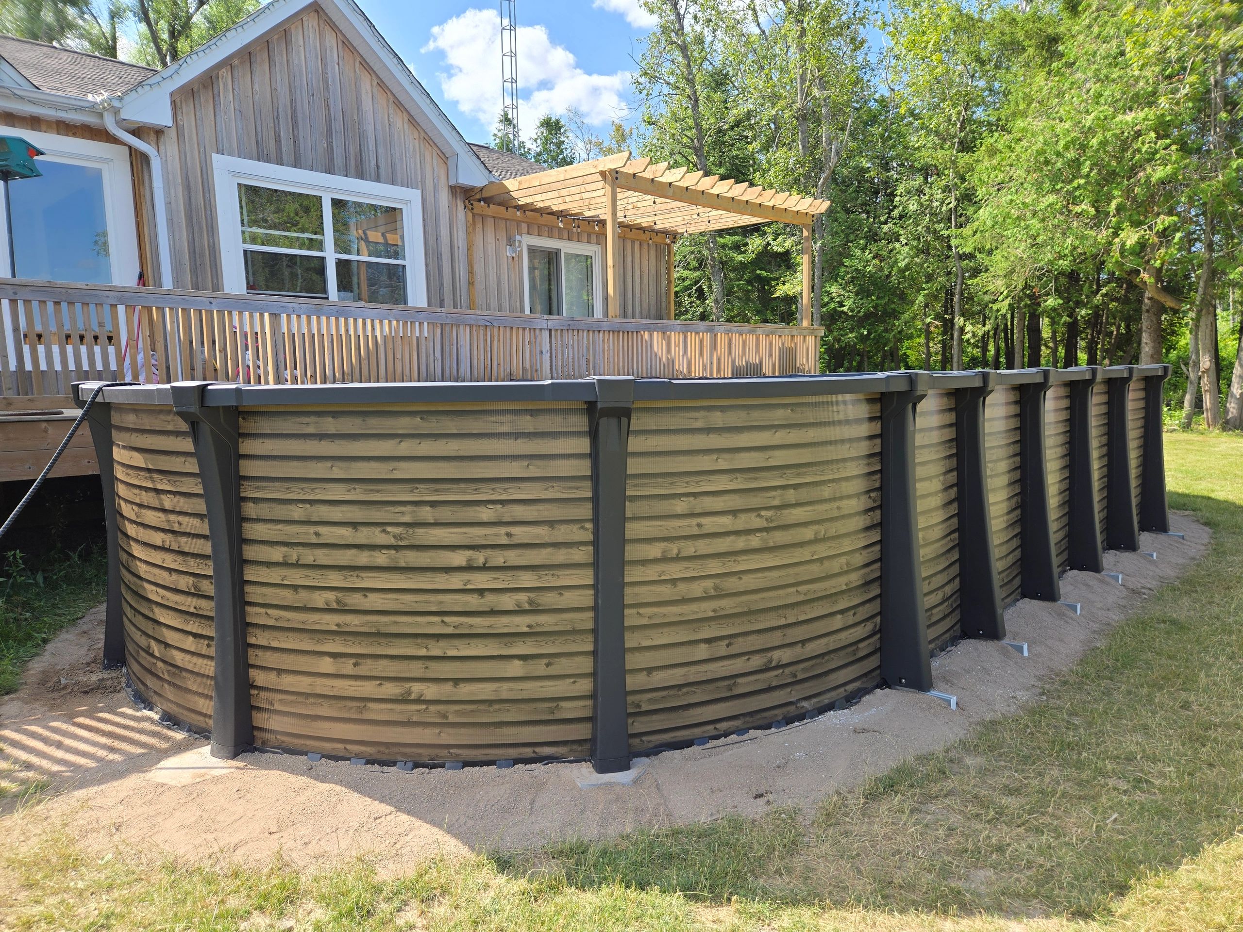 Above-ground carvin wooden pool next to a house with a wooden deck and pergola.Simcoe County ,Ontario