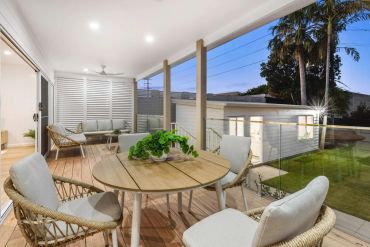 Modern outdoor patio with comfortable seating and a wooden table overlooking a garden.