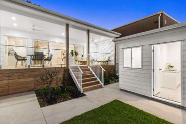 Modern backyard patio with stairs, glass railing, and outdoor seating area.